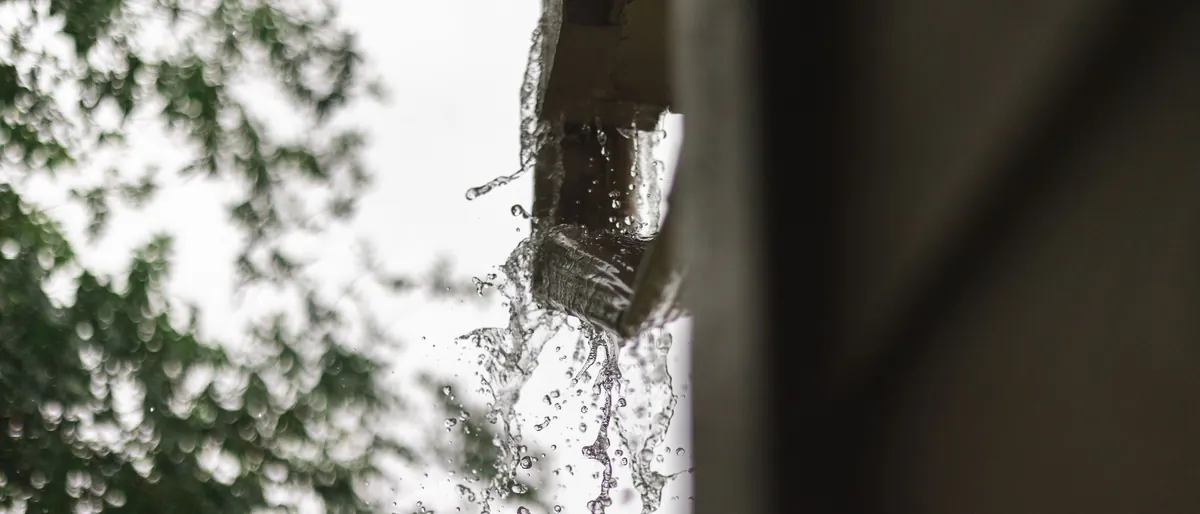 Regenwasser läuft über eine verstopfte Dachrinne und fällt in Tropfen herab