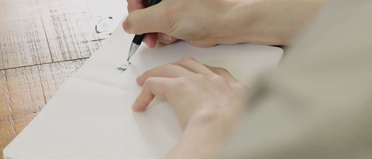 Two hands writing with a pen in an open notebook on a wooden table
